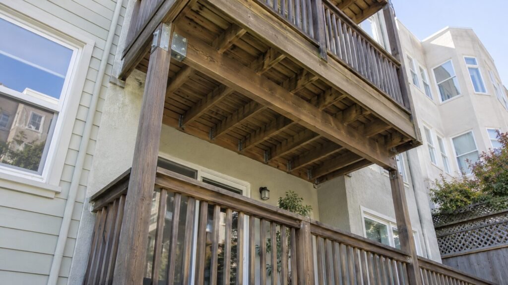 Joists, beam and galvanized post connector under a stacked wood balcony, framing checked in a Section 604 inspection