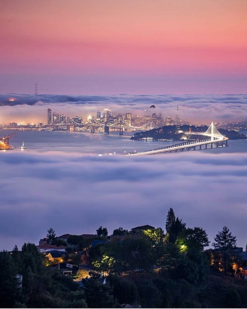 Oakland skyline and the new East Span of the Bay Bridge viewed from the Oakland Hills above the fog line — landmark in ABD Inspections Bay Area deck and balcony service area