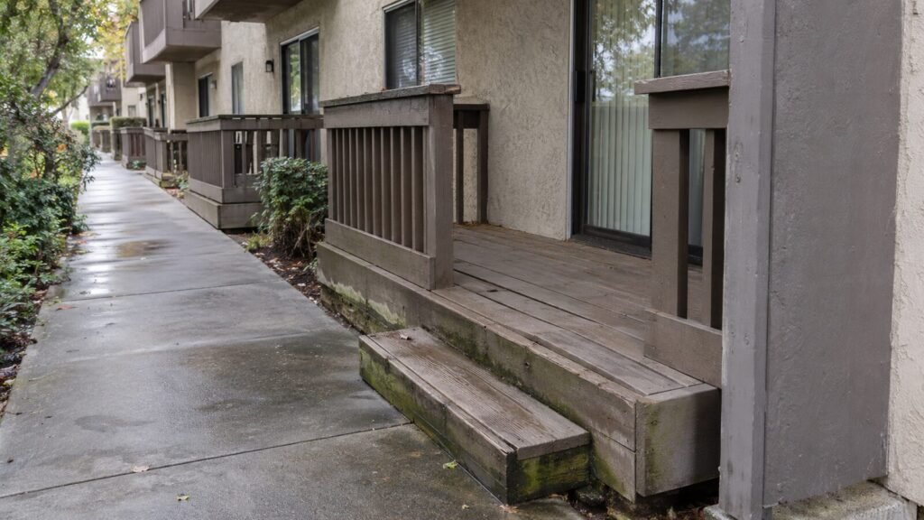 Rain-soaked wooden deck with moss on the step and skirt boards at a Sacramento apartment, a deck inspection red flag