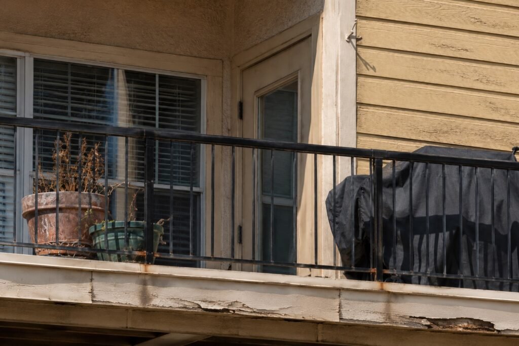 Condominium balcony with a black metal railing, peeling paint and water damage on the fascia below the deck edge — typical findings of an HOA balcony inspection in Sacramento