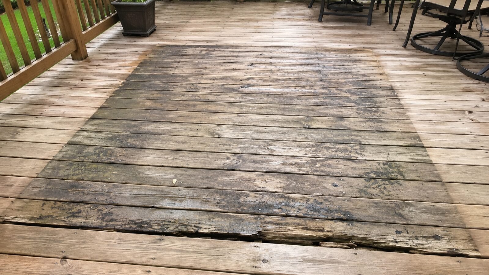 Dark rectangular stain left on deck boards where an outdoor carpet sat, with a rotted board edge