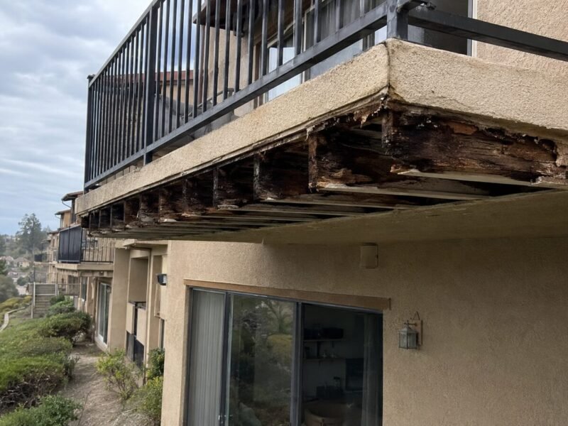 Open stucco soffit revealing decayed cantilever joist ends at the wall line