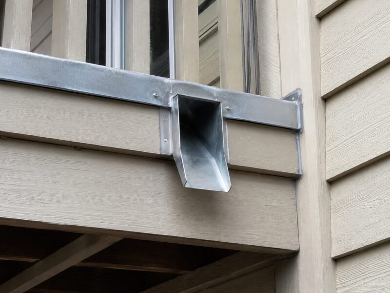 Extended and re-flashed scupper carrying discharge clear of the structure