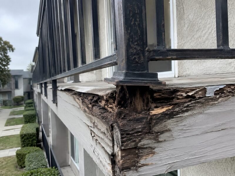 Guardrail post pulling free from a water-damaged rim joist at a Stockton apartment balcony
