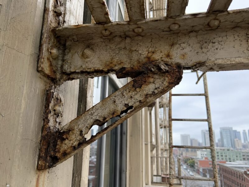 Corroded fire escape landing bracket with visible section loss before repair