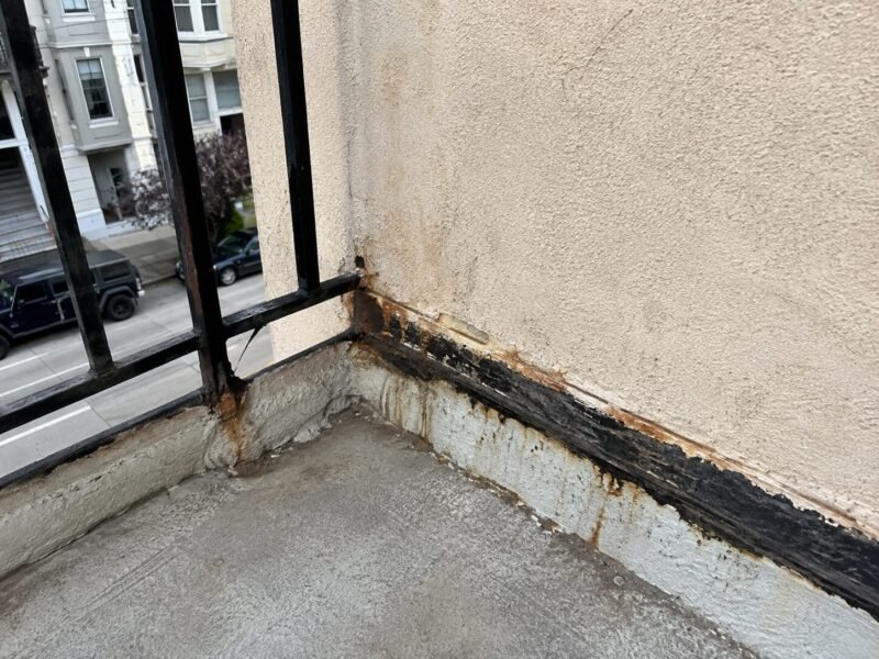 Painted-over balcony ledger flashing with water staining before repair