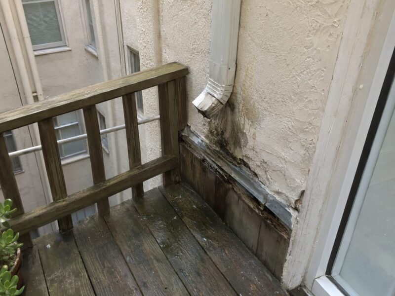 Downspout discharging into a light well directly above a hotel balcony ledger